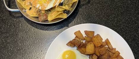 A plate with two fried eggs and a steak, and a bowl of nachos with cheese and jalapeños.