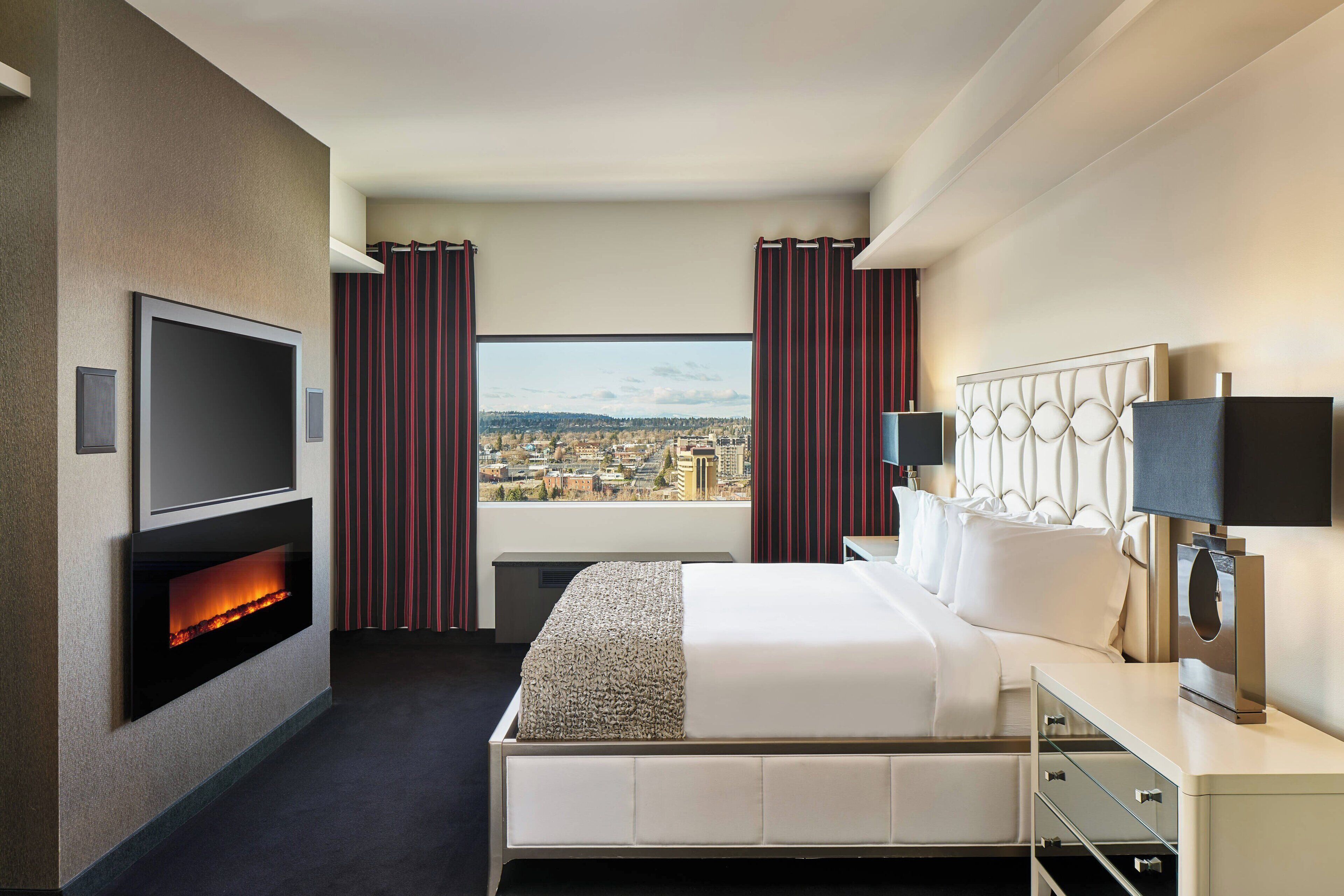 A hotel room with a bed, a TV, a fireplace, a city view, and curtains.