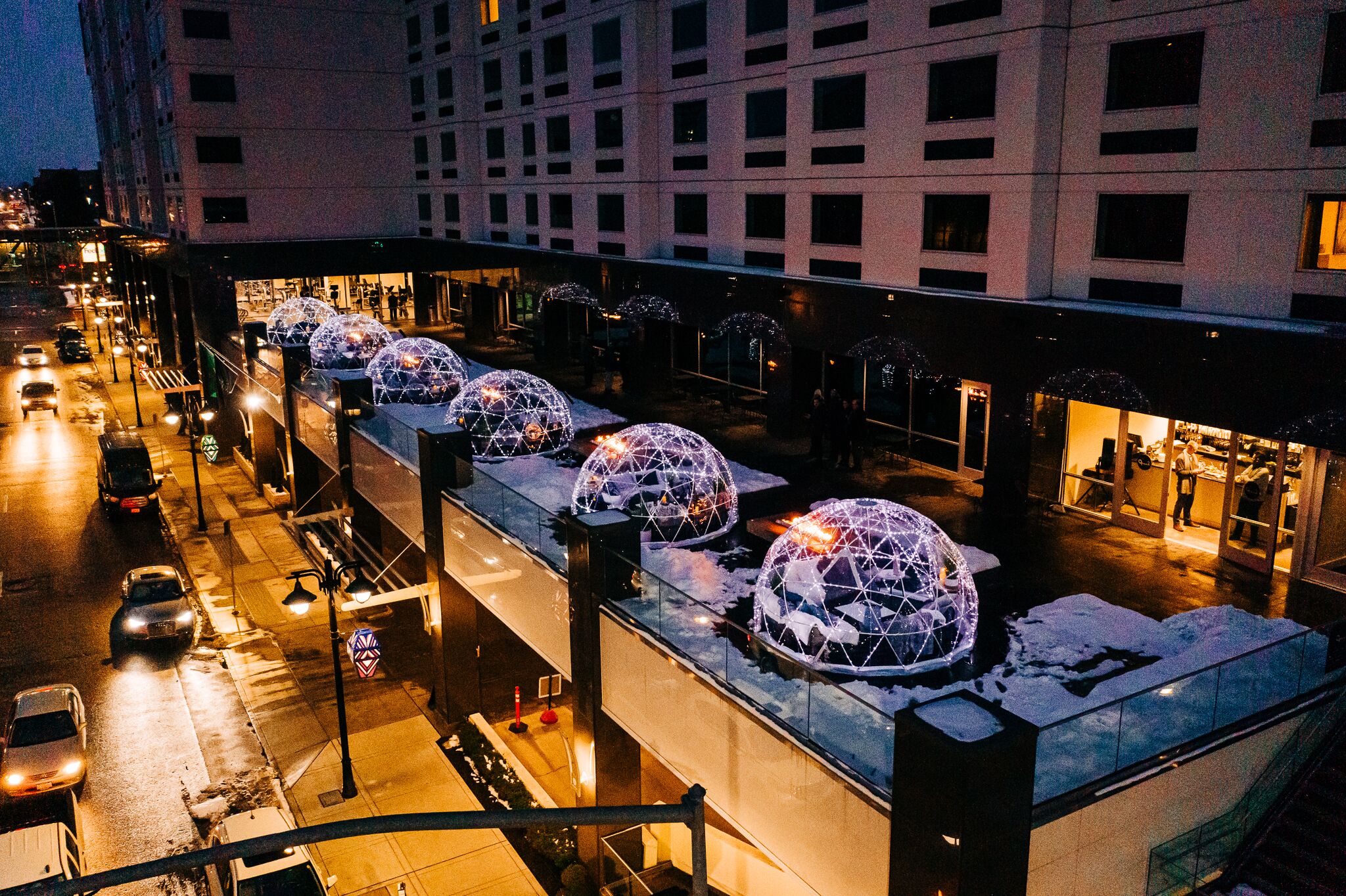 Un hotel de diseño moderno, con estructuras esféricas en el techo, un área exterior cubierta y vistas a la calle con coches y un paso de peatones.