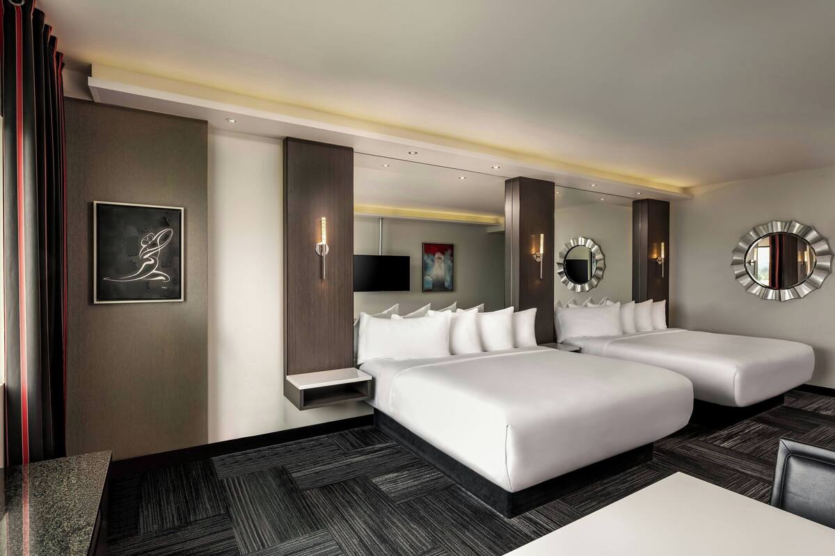A hotel room with two beds, a flat-screen TV, a framed artwork, and a mirror on the wall.