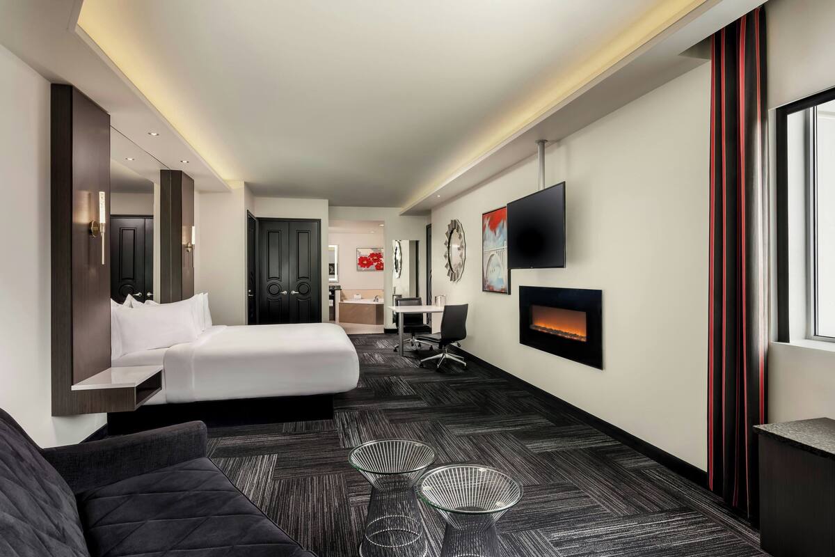 A hotel room with a bed, a desk, a TV, and a fireplace.