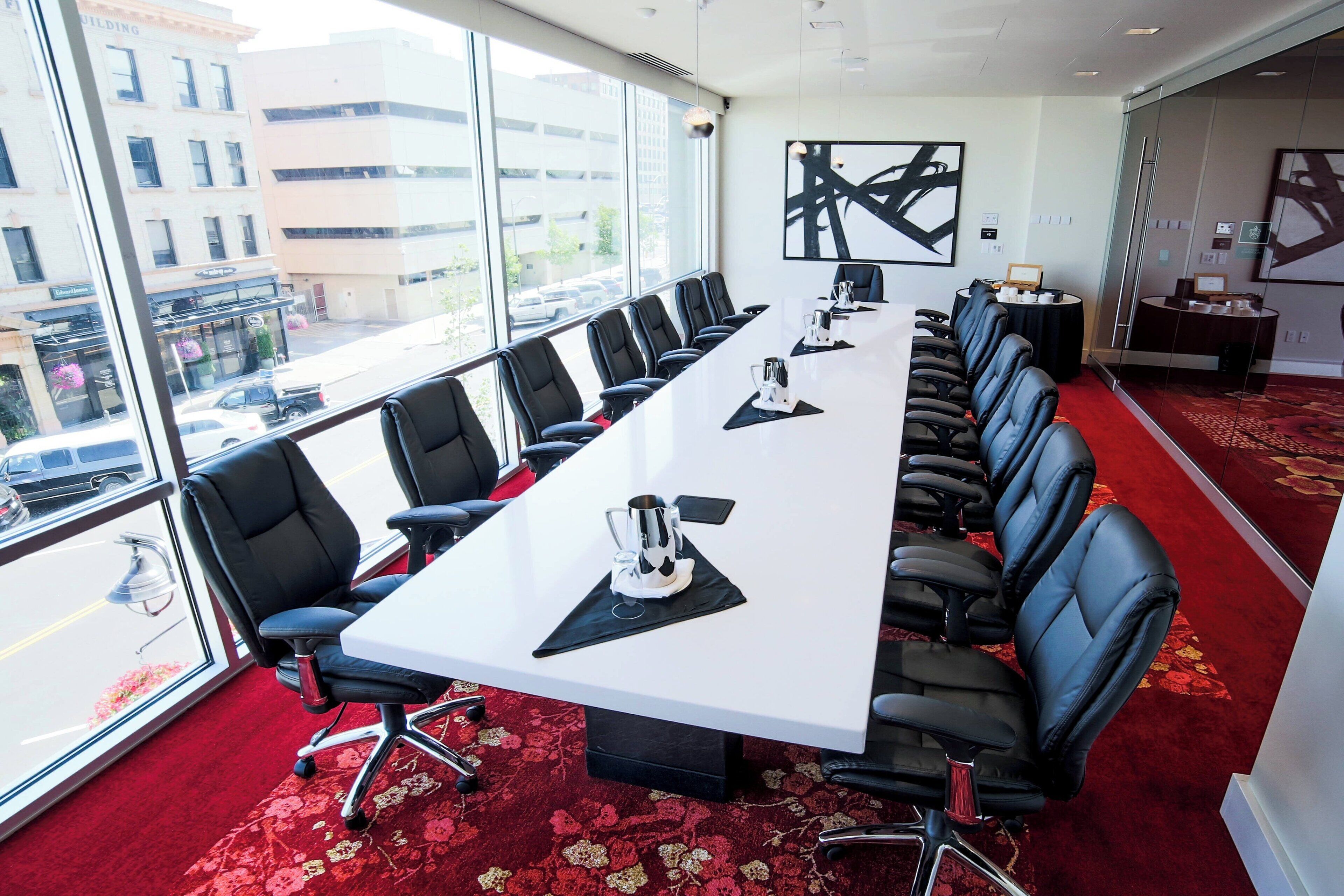 Een vergaderzaal met een lange tafel, zwarte stoelen en een rood tapijt.