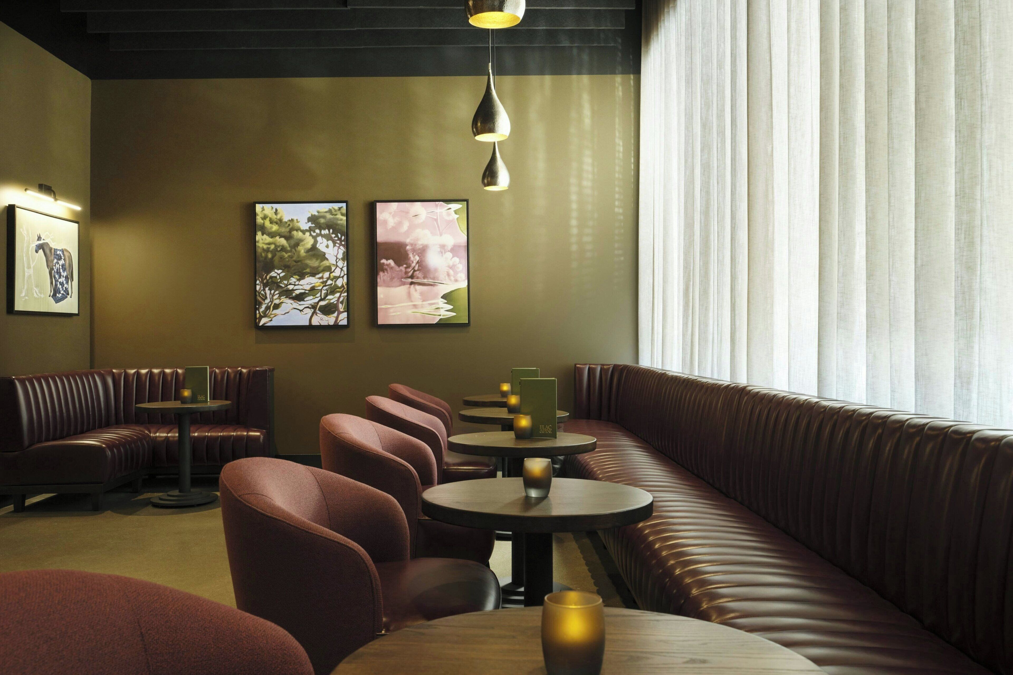 A restaurant interior with leather booths, round tables, and pendant lighting.