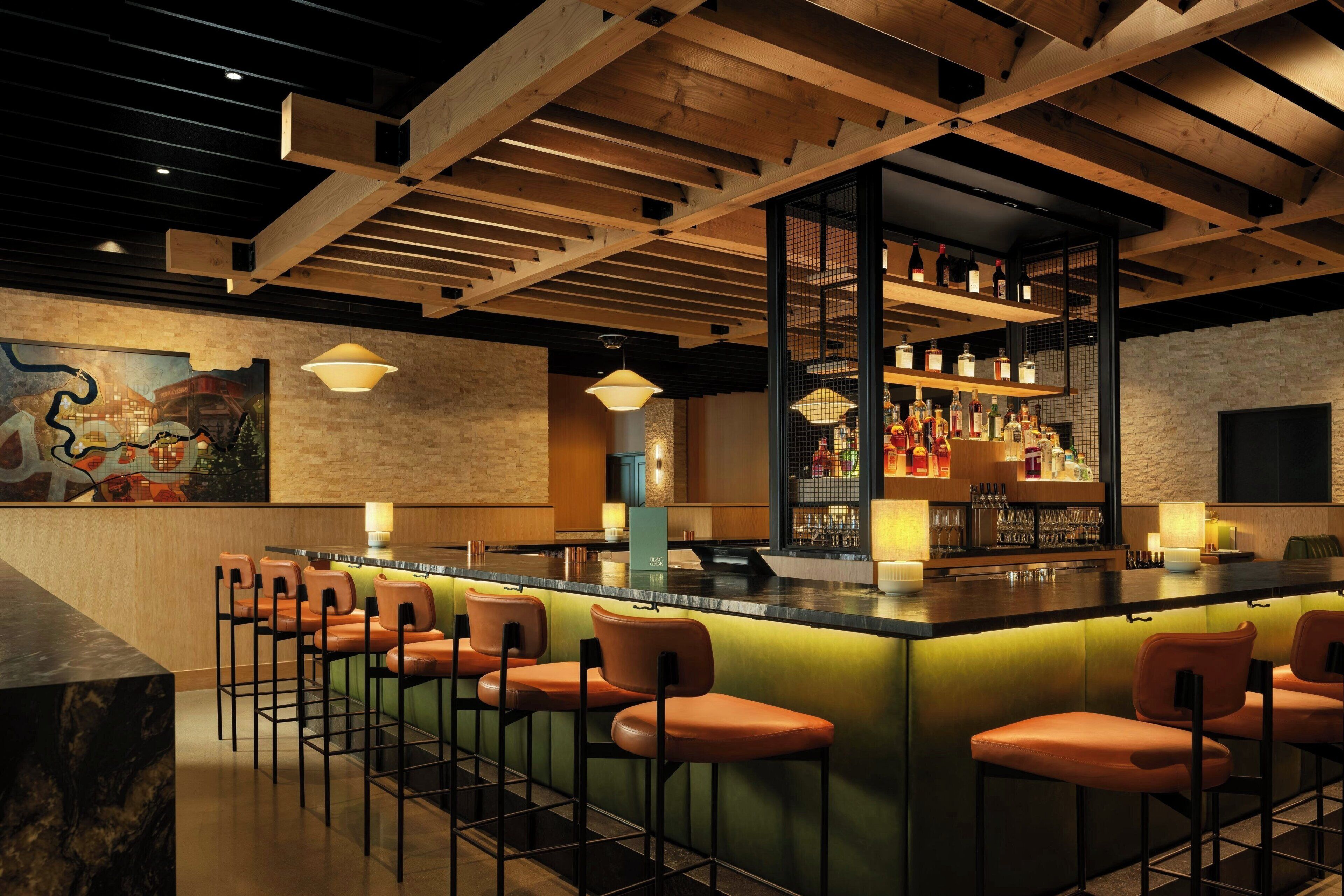 A bar area with a long counter, multiple stools, and a variety of bottles and glasses.