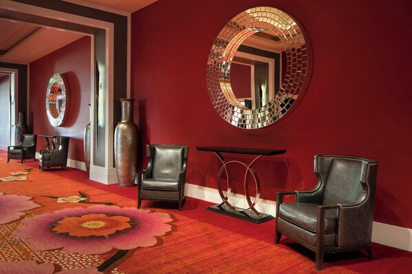 A lobby with red walls, a large mirror, two leather armchairs, a small table, and a floral carpet. - The Davenport Grand, Autograph Collection (Spokane)