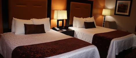 A hotel room with two beds, each with a headboard, bedside tables, lamps, and a framed picture on the wall.