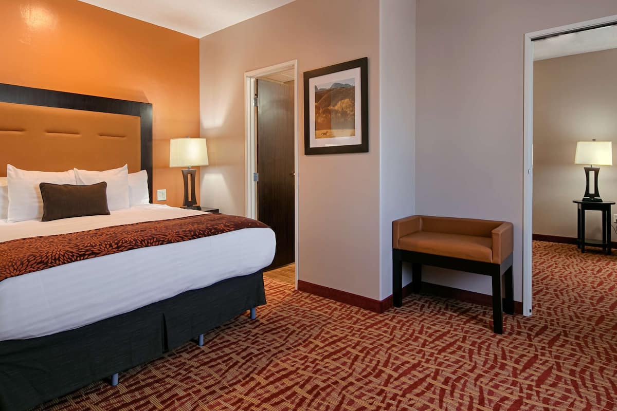 A hotel room with a large bed, two bedside lamps, a small armchair, and a framed picture on the wall.
