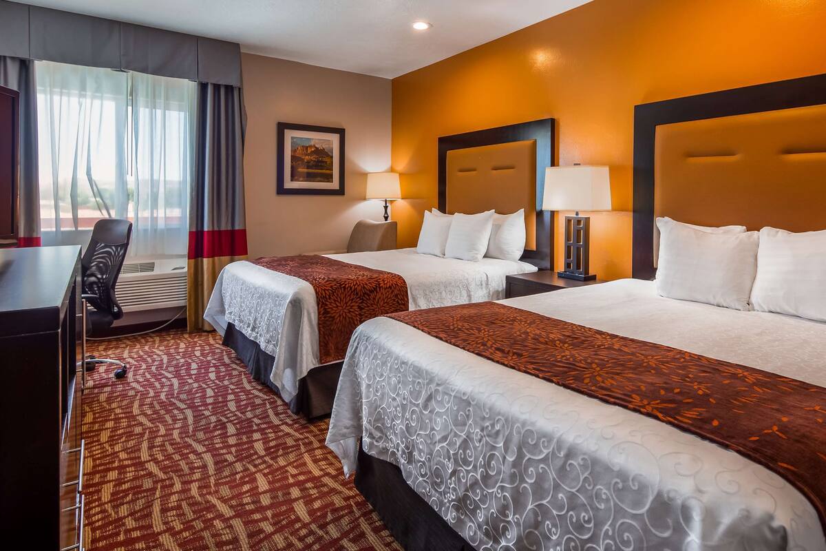 A hotel room with two beds, a desk, and a chair.