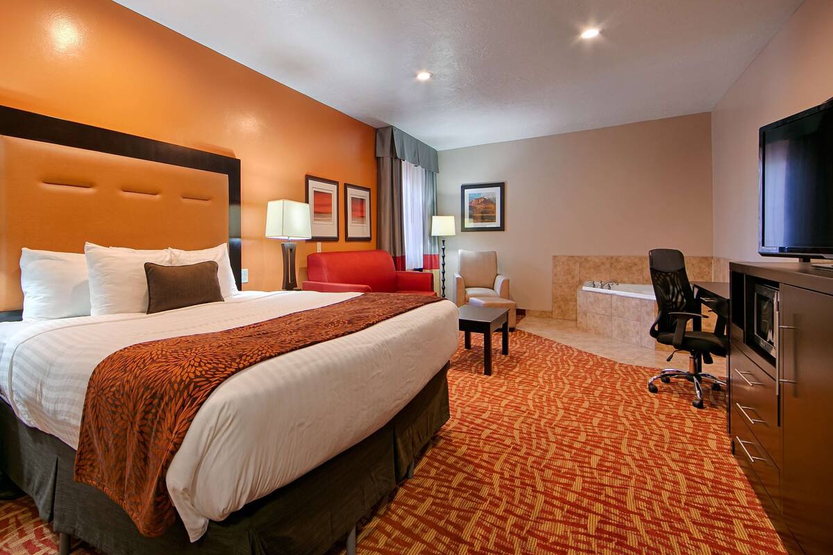 A hotel room with a large bed, a desk, a chair, a TV, and a bathroom.
