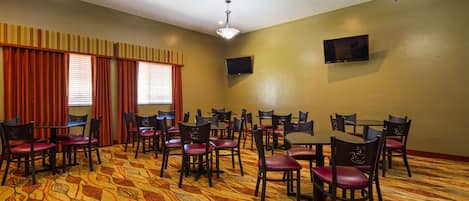 A conference room with multiple tables and chairs, a flat-screen TV mounted on the wall, and a patterned carpet.