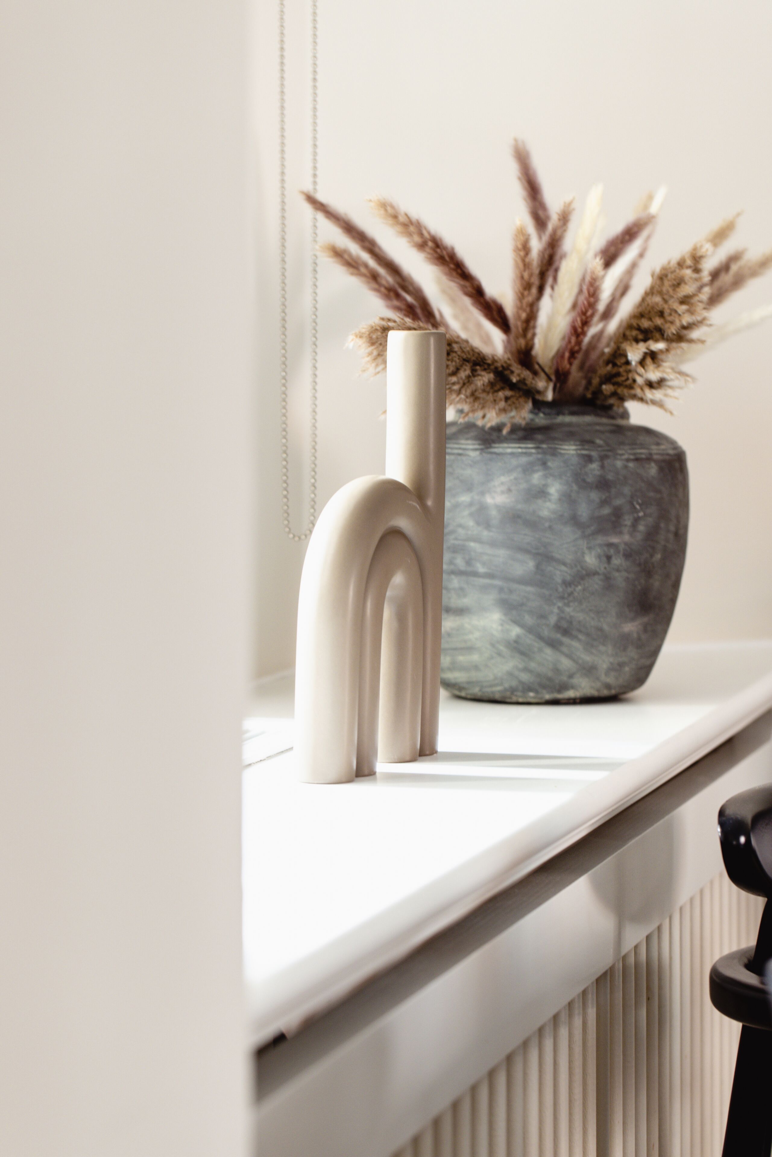 Een witte radiator, een vaas met gedroogde planten en een wit object op een witte plank.