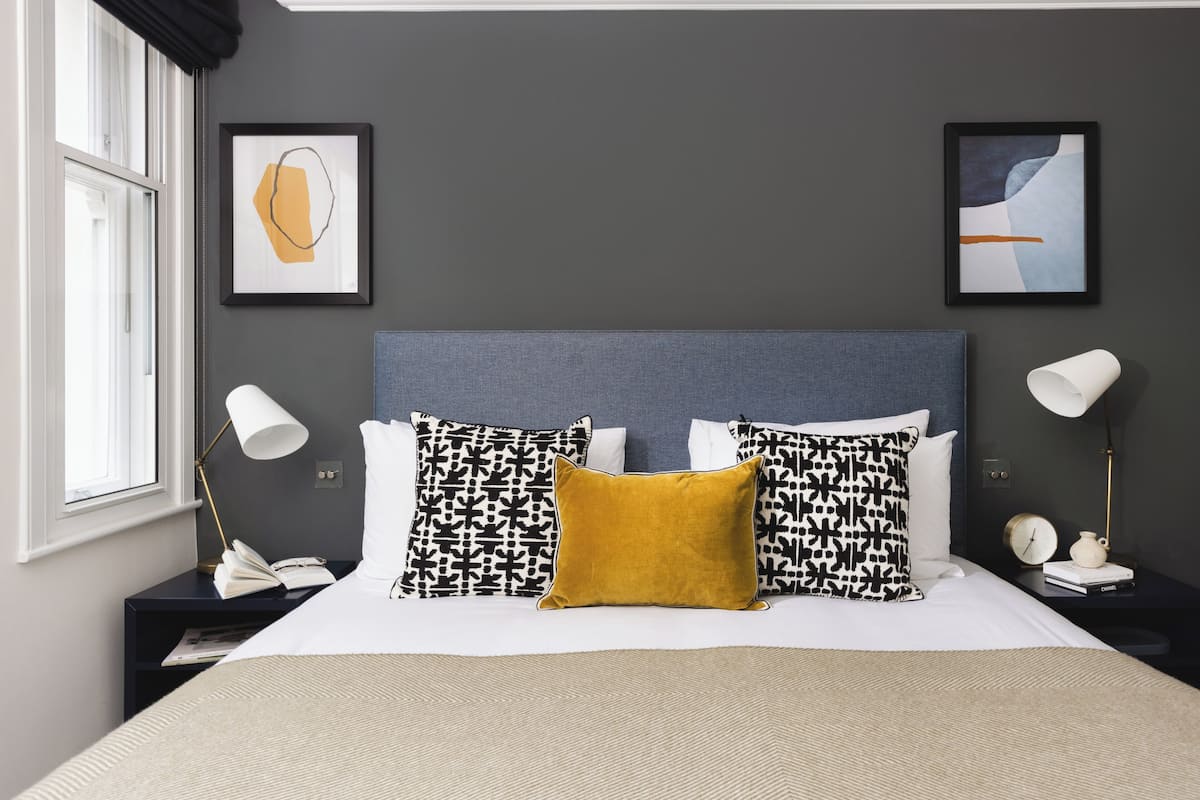 Un dormitorio ordenado con una cama, dos mesitas de noche y dos lámparas de pared.