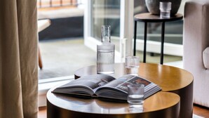 A round wooden table with a metallic base, a book, and a glass bottle. - Native Mayfair (London)