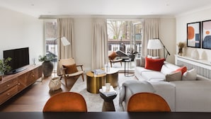 A modern living room with a sofa, armchairs, a coffee table, and a TV on a wooden cabinet. - Native Mayfair (London)