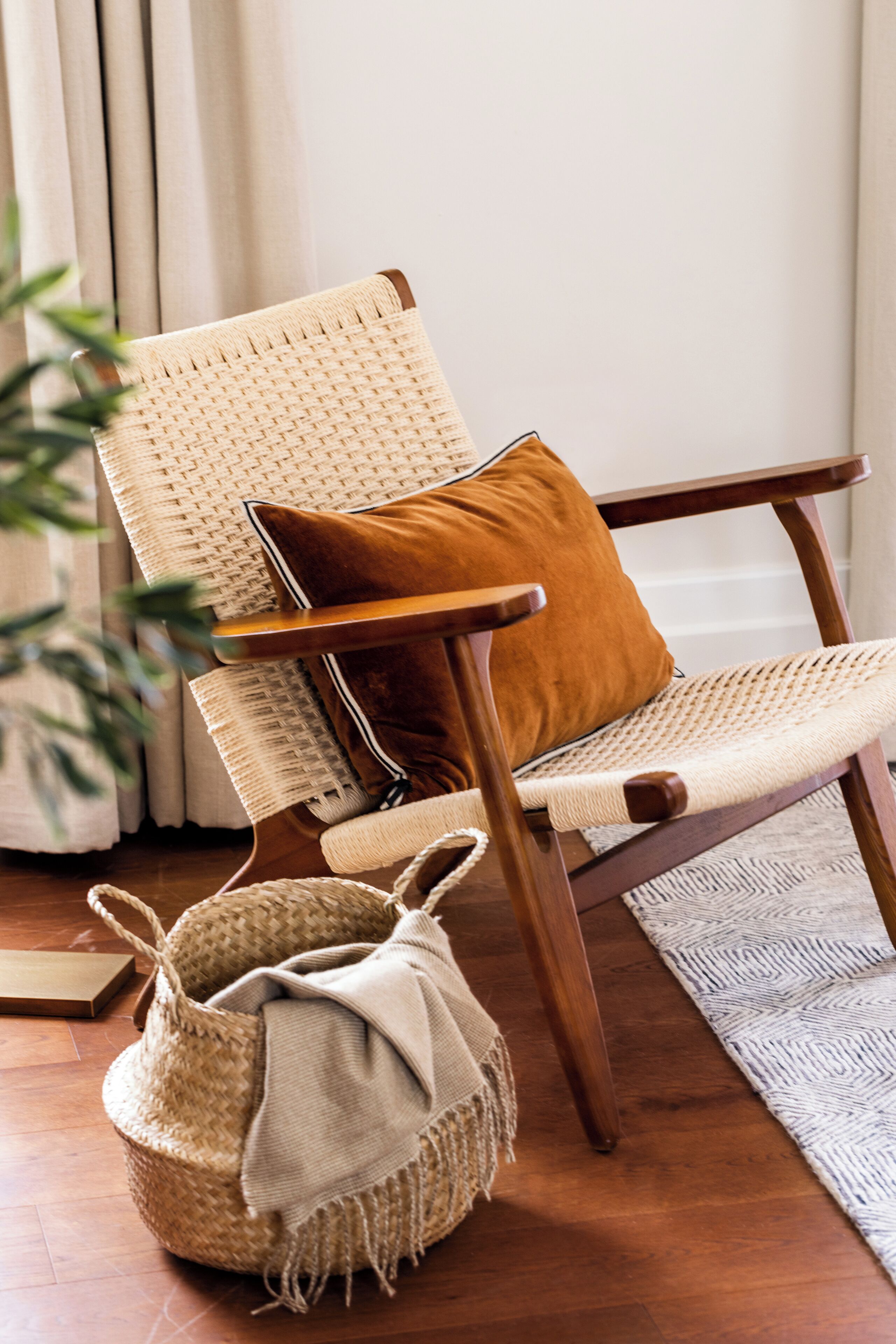 Una silla de madera con respaldo trenzado y un cojín marrón, sobre un piso de madera cubierto con un tapete tejido.