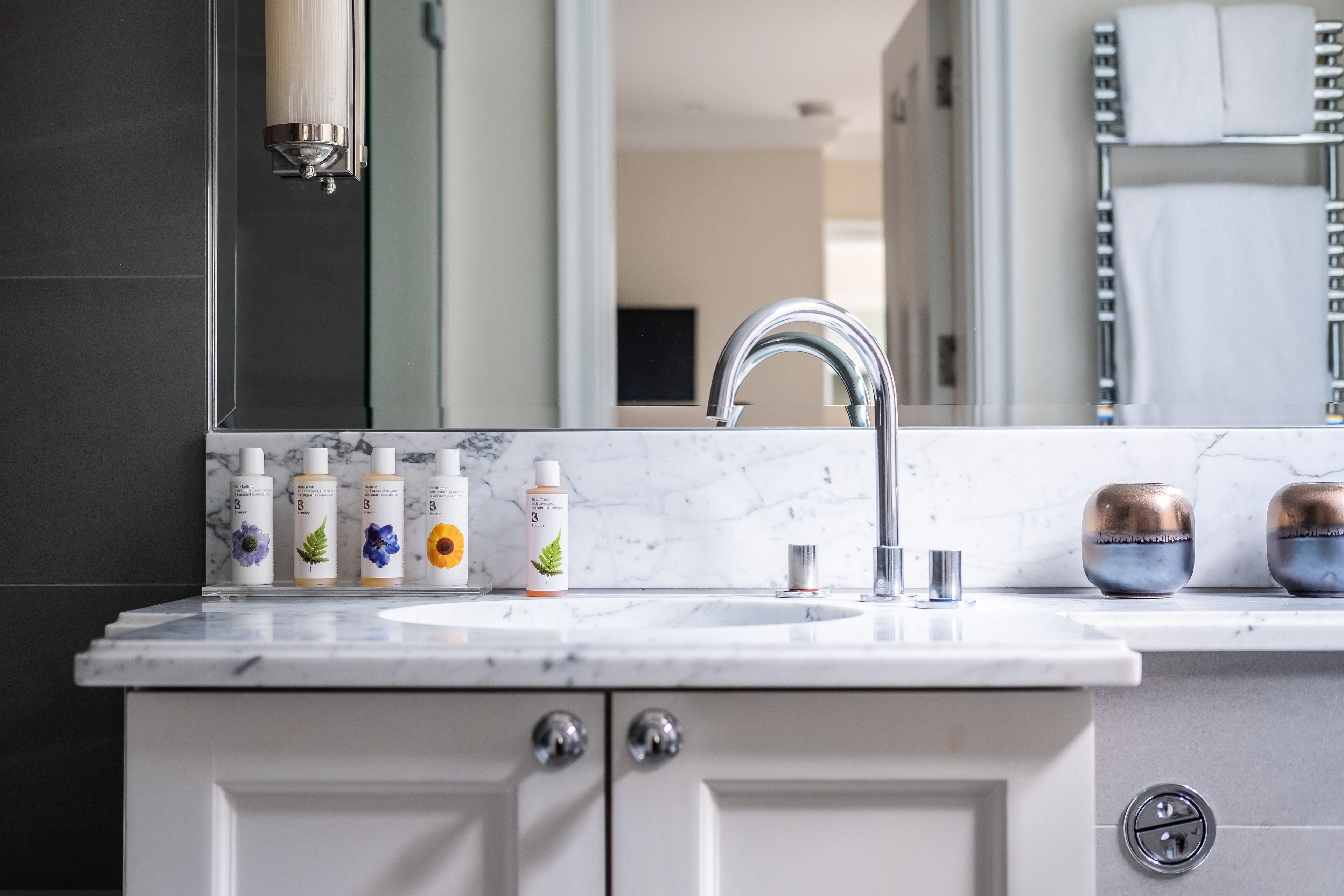 A bathroom with a white marble sink, a modern faucet, and a mirror above it. There are four bottles of toiletries on the sink.