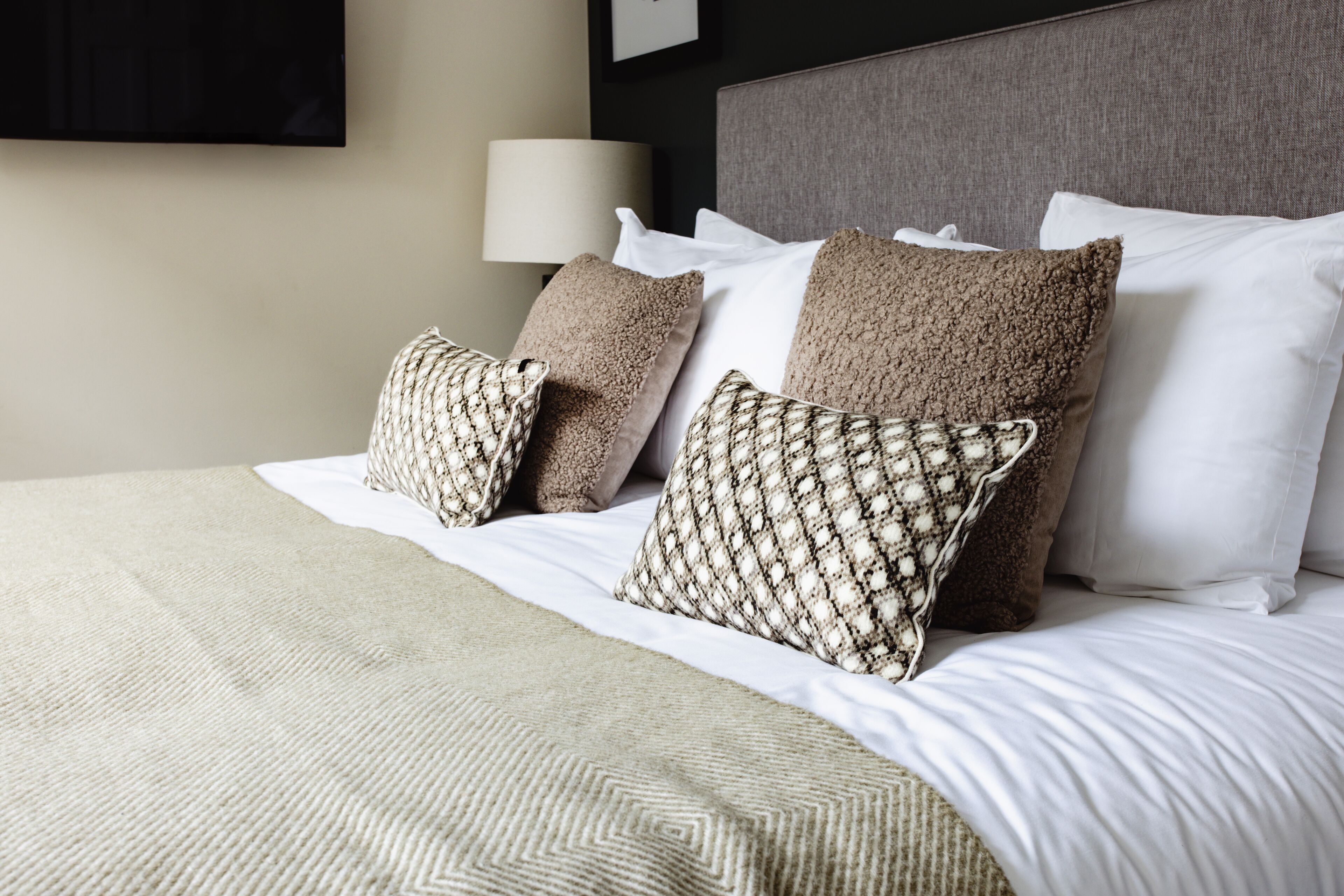A neatly made bed with a patterned throw blanket, multiple pillows, and a headboard.