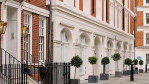 A row of white brick buildings with arched windows and a black metal fence in front. - Native Mayfair (London)