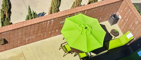 A patio area with a green umbrella, outdoor furniture, and a brick wall.
