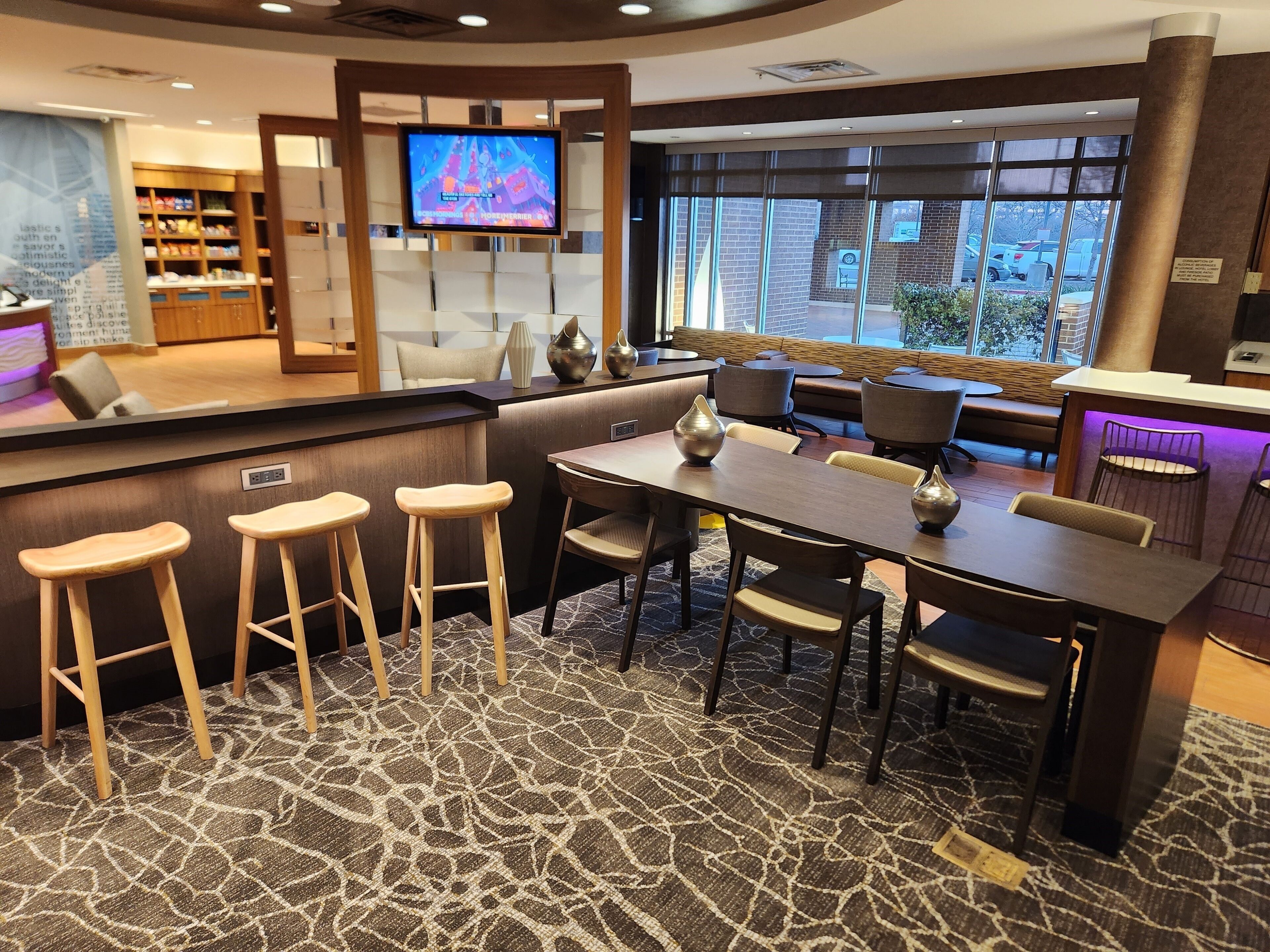 A modern hotel lobby with a bar area, seating arrangements, and a television screen.