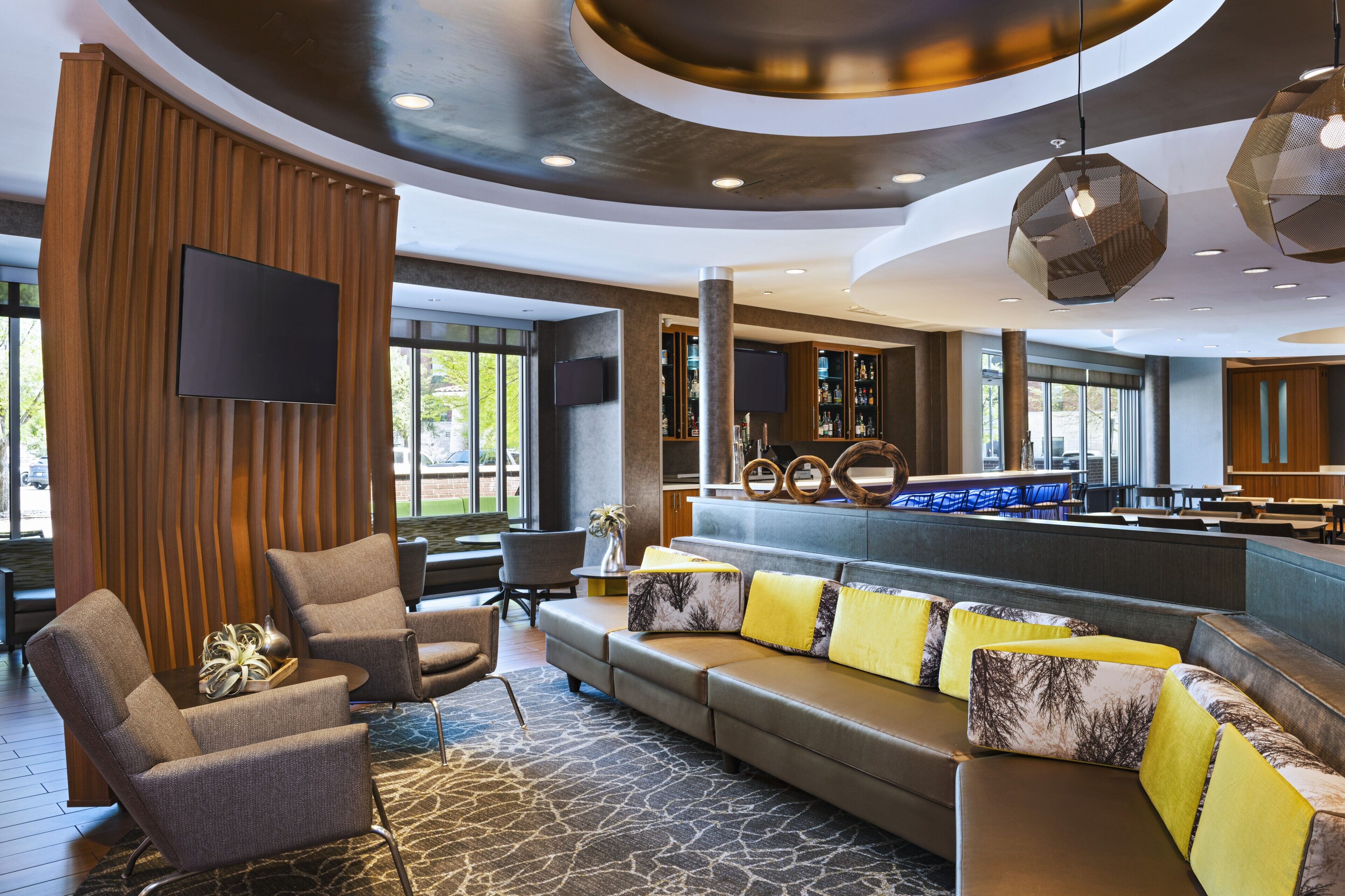 A modern hotel lobby with a seating area, a bar, and a large window providing a view of the outdoors.