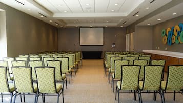 Un salón de conferencias con filas de sillas, una pantalla de proyector y una pared decorada con adornos circulares de colores.