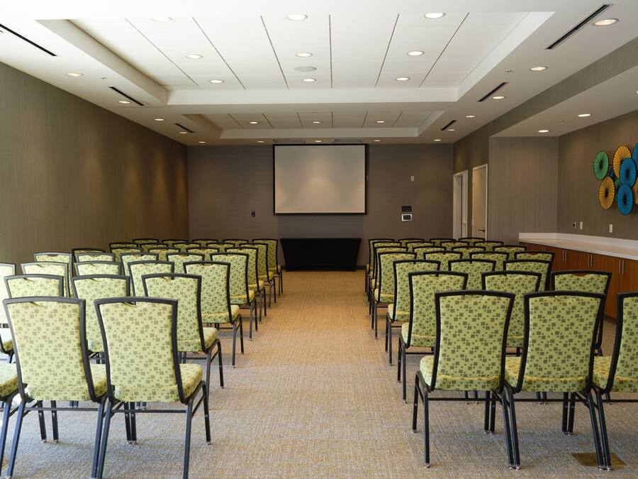 Un salón de conferencias con filas de sillas, una pantalla de proyector y una pared decorada con adornos circulares de colores.