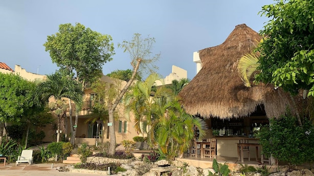 A pool area with a thatched-roof structure, palm trees, and a stone pathway. - Villas Bakalar (Bacalar)