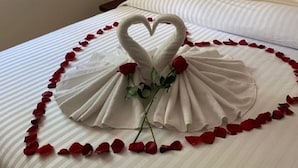 A bed with a heart-shaped towel arrangement and rose petals, a white headboard, and a striped bedspread. - Villas Bakalar (Bacalar)