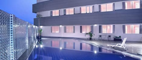 Un hotel moderno con piscina infinita en la azotea, barandilla de vidrio y terraza con asientos.