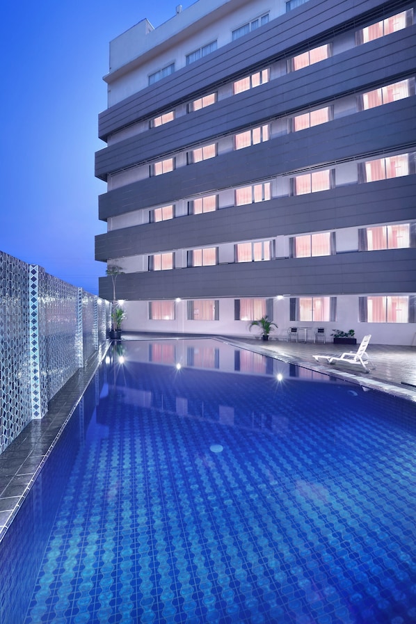 A modern hotel with a rooftop infinity pool, a glass fence, and a terrace with seating.