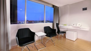 A modern hotel room with two black chairs, a small white table, a mini-fridge, and a window with a city view. - favehotel Jababeka Cikarang (Cikarang)