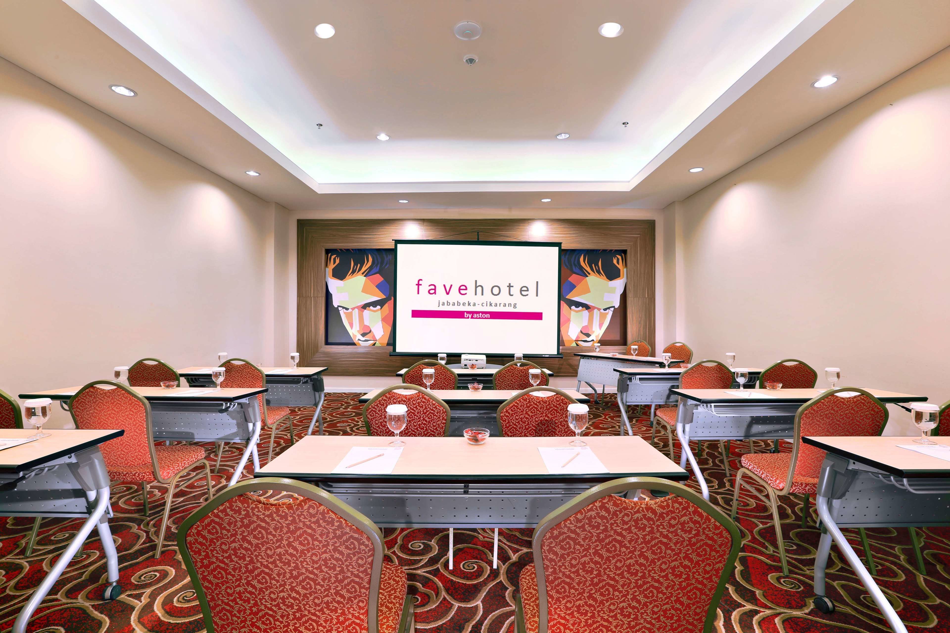 Un salón de conferencias con mesas, sillas y una pantalla grande que muestra 'favehotel'.