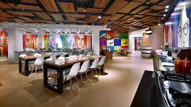 A modern restaurant with wooden ceiling panels, colorful murals, and a central dining area with tables and chairs. - favehotel Jababeka Cikarang (Cikarang)