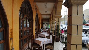 An outdoor cafe with tables and chairs, a tiled floor, and a street view. - Hotel Arcos del Parque (Acayucan)