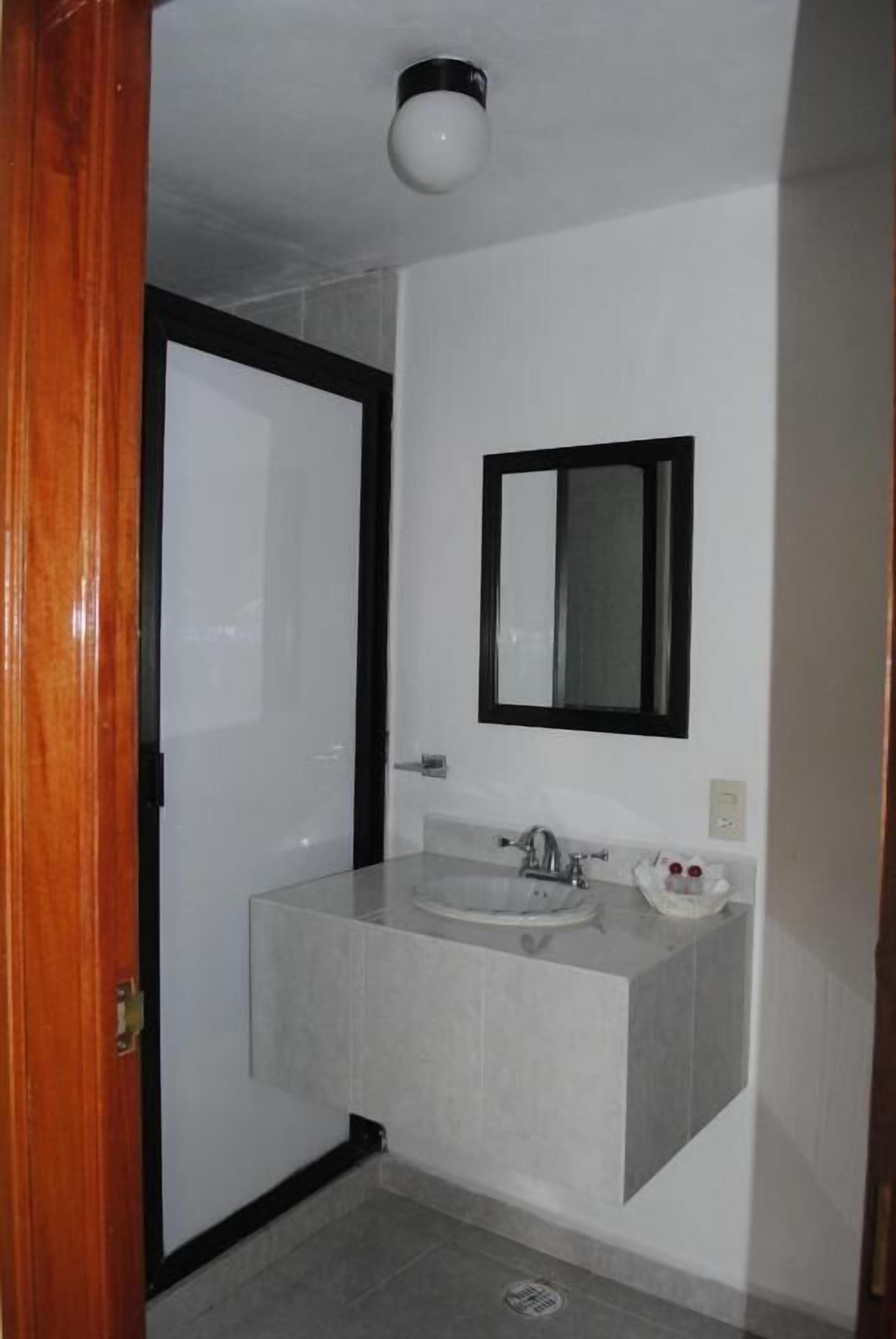 Un baño con un lavamanos blanco, un espejo con marco negro y una puerta blanca.