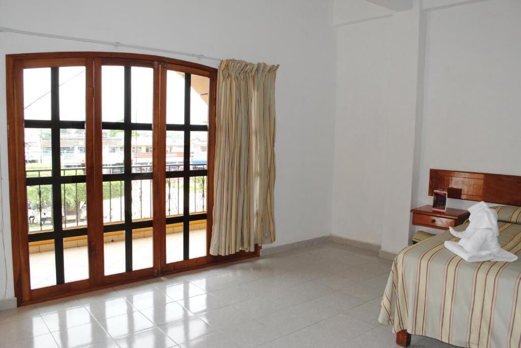 A hotel room with a large sliding glass door leading to a balcony, a bed with a striped bedspread, a bedside table, and a nightstand.