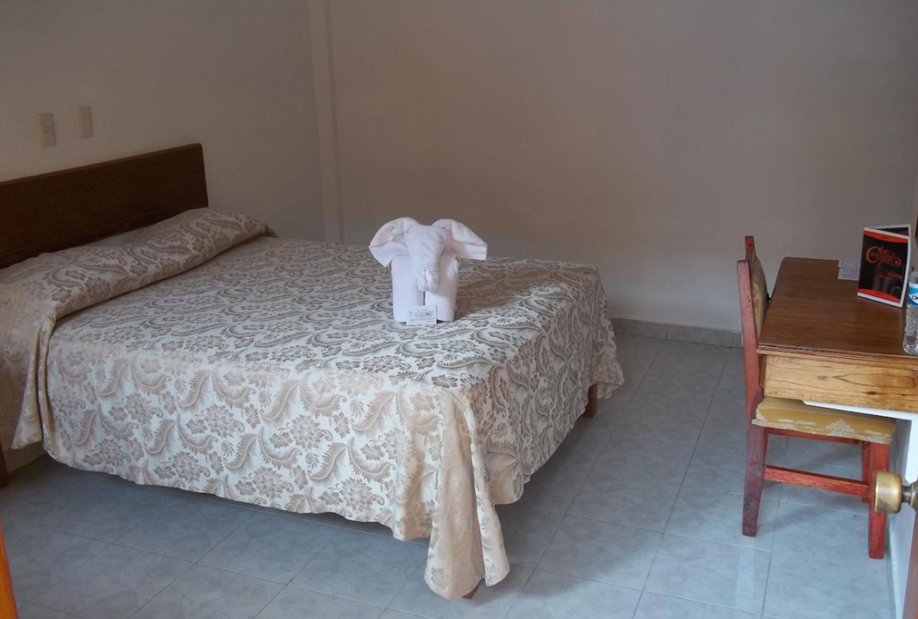 A hotel room with a bed, a wooden chair, and a small table with a book.