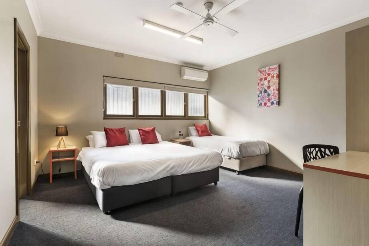 A hotel room with a large bed, a desk, a chair, a lamp, and a ceiling fan.
