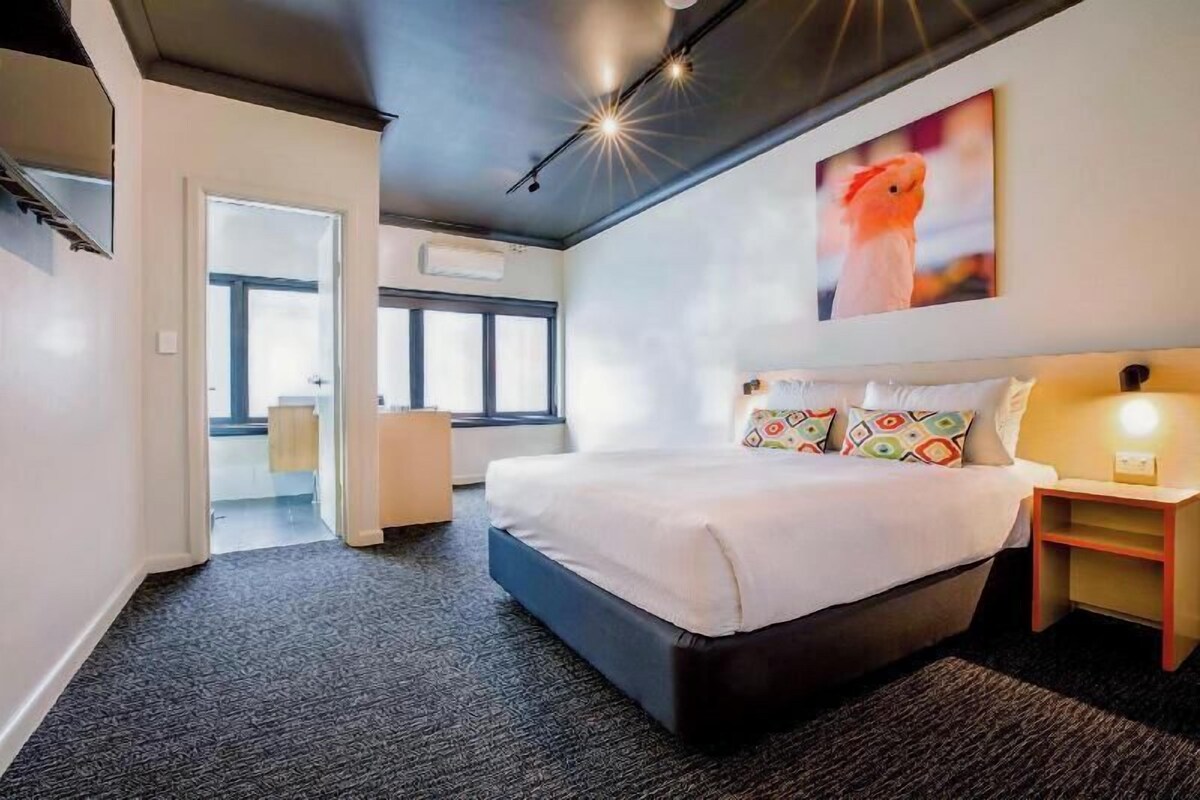 Une chambre d’hôtel moderne avec un grand lit, une table de chevet, une lampe fixée au mur et une fenêtre.