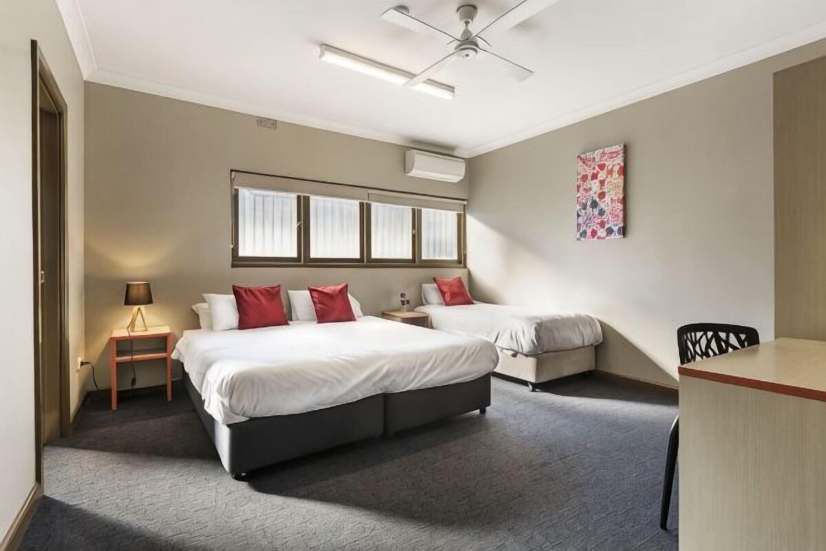 A hotel room with a large bed, a desk, a chair, a lamp, and a ceiling fan.