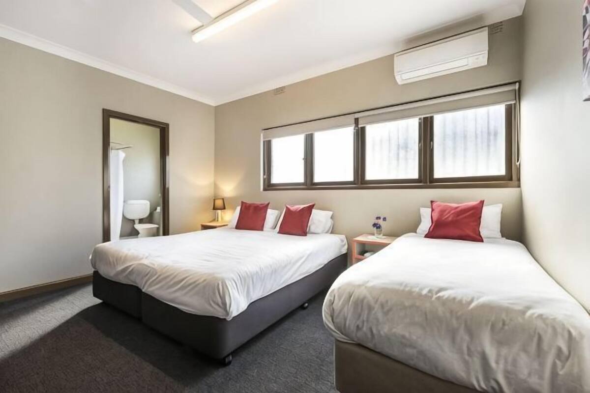 A hotel room with two beds, a window, a nightstand, and a mirror.