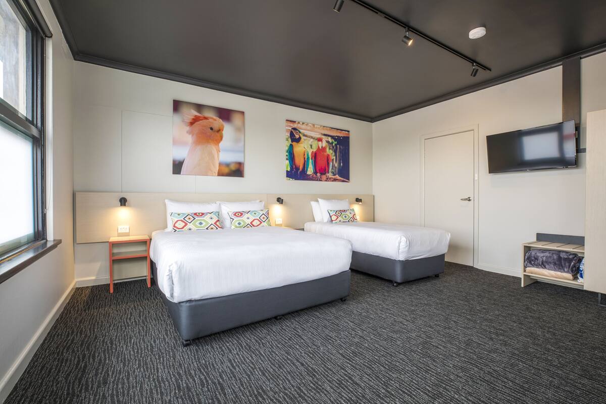 A hotel room with two beds, a flat-screen TV, and artwork on the wall.