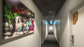 Um corredor de hotel longo, com portas numeradas 15 e uma grande pintura abstrata na parede esquerda.