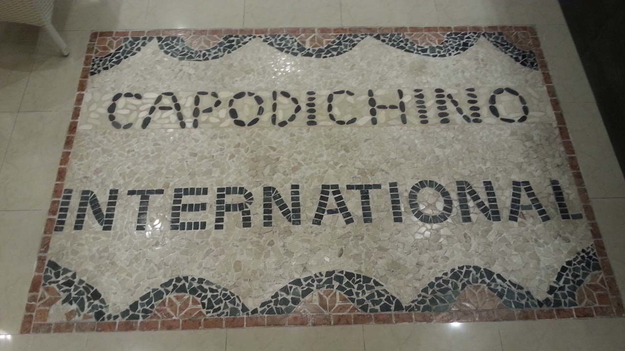 Een mozaïekvloer met de woorden 'CAPODICHINO INTERNATIONAL' in zwarte tegels.