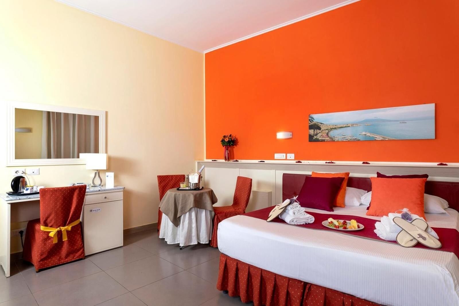 Ein Hotelzimmer mit Bett, Schreibtisch, Stuhl, einem kleinen Tisch mit einem Getränk und einem Bild an der Wand.