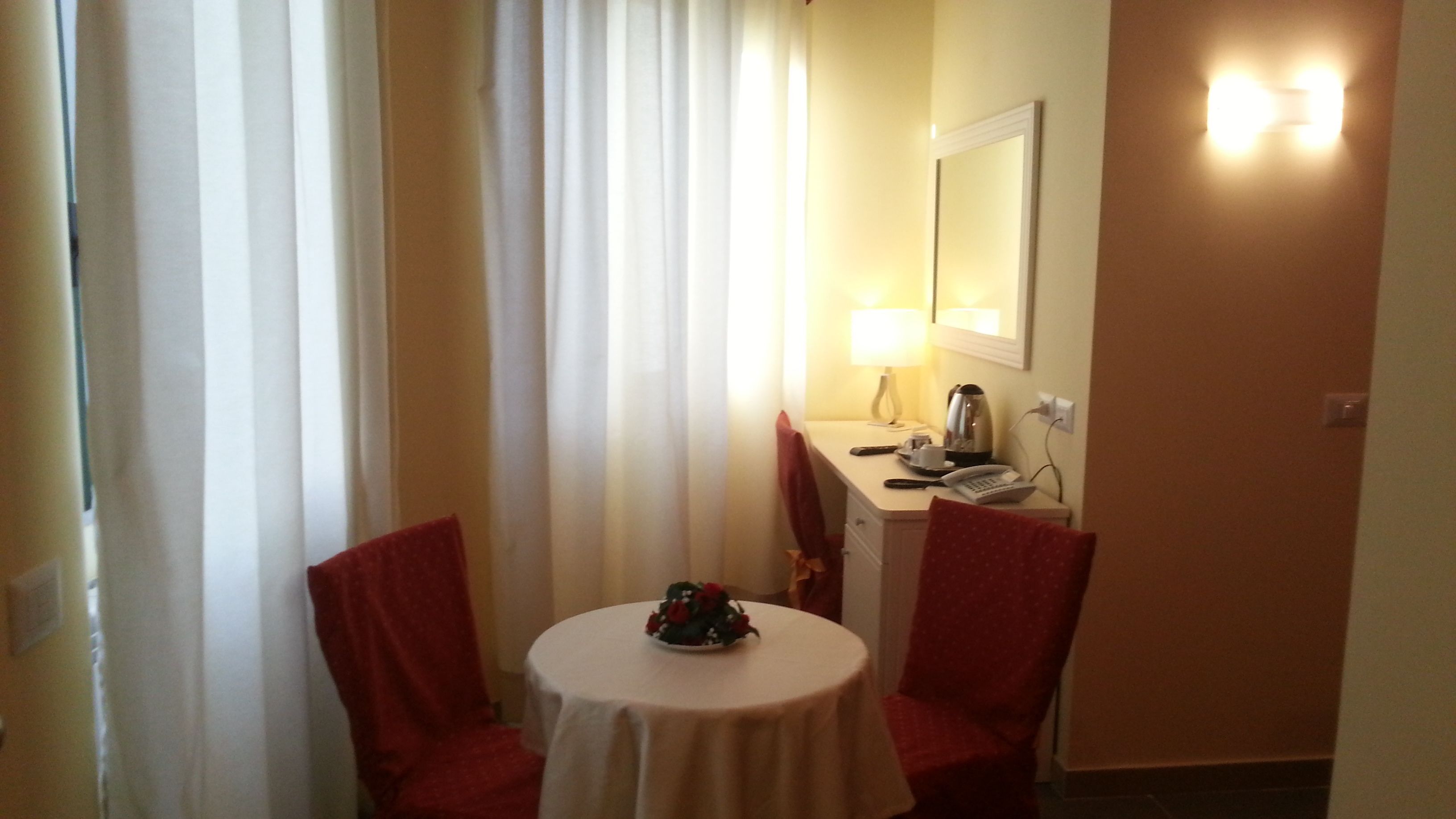 Habitación de hotel con una mesa redonda, dos sillas, un escritorio con lámpara, teléfono y un espejo en la pared.