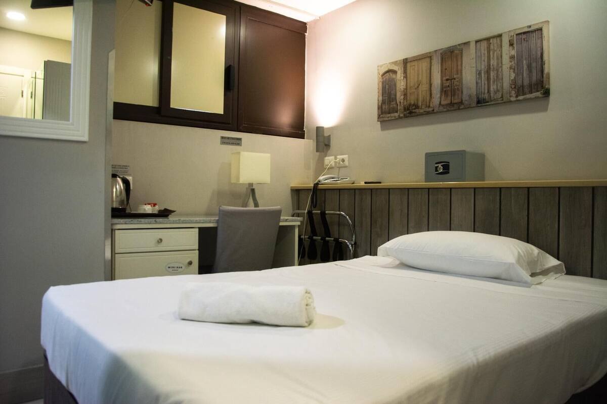 A hotel room with a bed, a desk with a chair, a telephone, and a wall-mounted artwork.