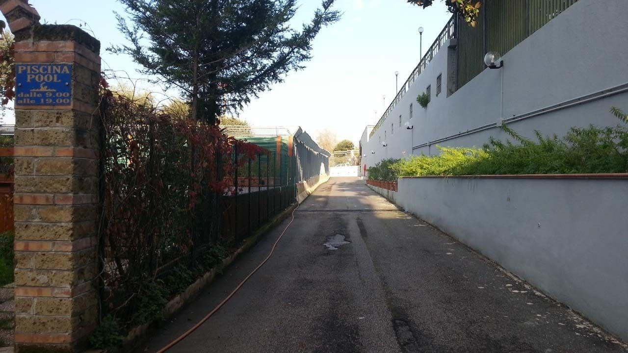 Egy keskeny sikátor, melynek bal oldalán téglából épült fal, jobb oldalán pedig egy fehér épület áll. A bal oldali falon egy úszómeddére utaló tábla látható.