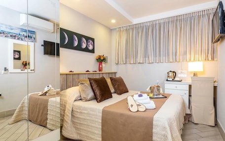 A hotel room with two beds, a desk, a chair, a TV, a painting of moons, and a window with curtains.